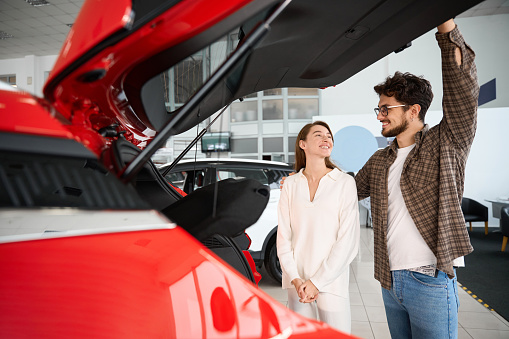 Satisfied man and woman buying new automobile in dealership looking at car opening trunk