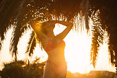Caucasian woman tying up her hair, while enjoying the sunset under the palm tree on her vacation