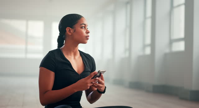Portrait of young African American sporty young woman sits on floor, using yoga online fitness training application to get the workout plan.