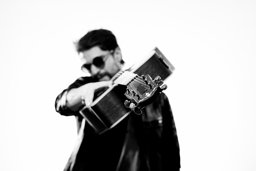 A man plays the guitar in a black leather jacket with sunglasses on a light background. High quality photo
