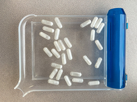 Hand pill counting tray with white pill capsules