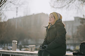 Asian Chinese woman with winter coat  knitted hat sitting in public park looking away during weekend morning