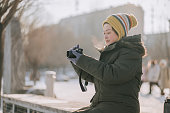 Asian Chinese woman with winter coat  knitted hat photographing in public park looking away during weekend morning