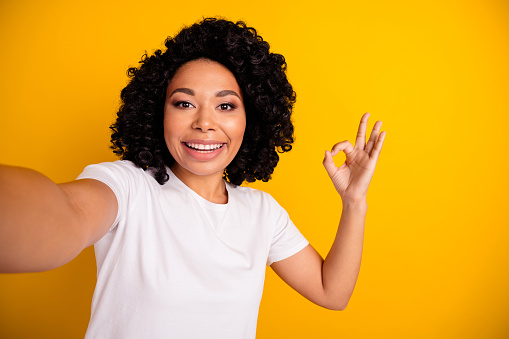 Photo of funky pretty lady dressed white t-shirt showing okey gesture recording video vlog isolated yellow color background.