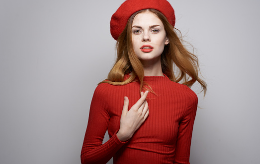 Beautiful woman in red sweater and hat cosmetics model gray background. High quality photo