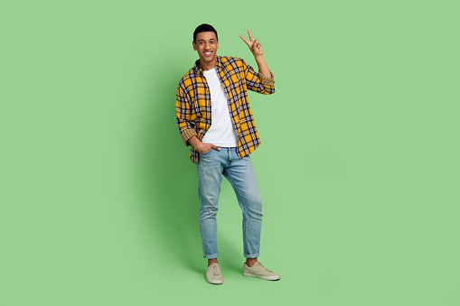 Full size photo of satisfied positive man arm fingers demonstrate v-sign empty space isolated on green color background.