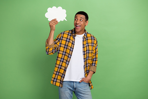 Photo of young positive guy holding paper bubble idea empty space genius proposition advertisement isolated on green color background.