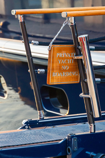 Luxury yacht entrance placard hanging on chrome chains at entrance gangplank, reading “Private yacht, no boarding”