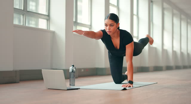 Woman does yoga on mat using laptop to watch video tutorial. Slow motion.
