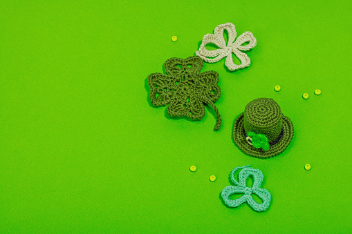 Handmade St. Patrick's Day concept. Traditional decorative symbols, pot with golden coins, crocheted four-leaf clover. Hard light, dark shadow, green background, top view