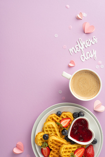 Mother's Day breakfast delight: overhead vertical photo showing heart waffles, strawberries, blueberries, marmalade, espresso on a soft purple background, space for text