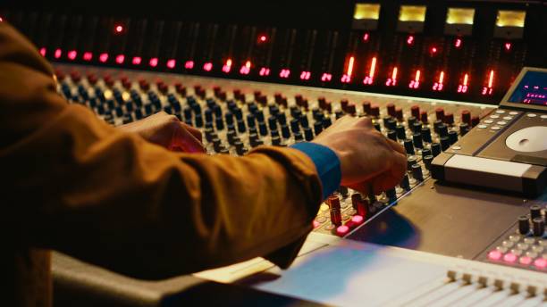 Audio technician producing new music at mixing console in control room, twisting knobs, pressing sliders and switchers. Producer working on processing and editing sounds quality. Camera A.