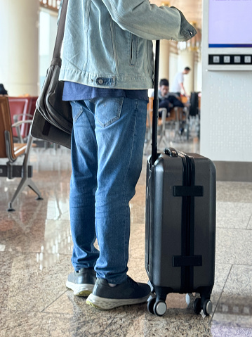 Stock photo showing close-up, rear view of wheelie suitcase being wheeled through an airport departure area.