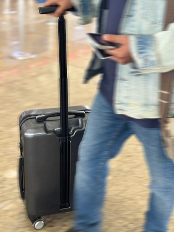 Stock photo showing close-up view of hotel guest wearing a rucksack and wheeling a suitcase through a luxury hotel reception.