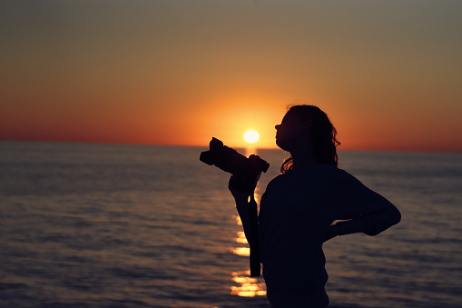 silhouette of a woman with a camera at sunset near the sea beach landscape. High quality photo