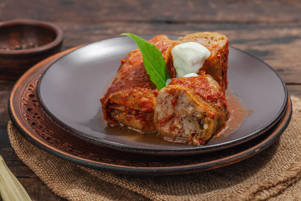 Cabbage rolls stuffed with rice and meat stewed in tomato sauce. Traditional dish, ready-to-eat food, sour cream. Old wooden background, close up