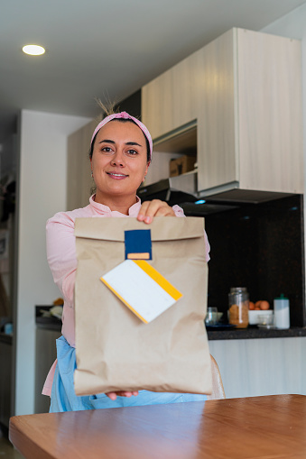 Latina businesswoman from Bogota Colombia between 30 and 34 years old, prepares the packaging where she will send her Italian food to clients wearing her uniform from her kitchen