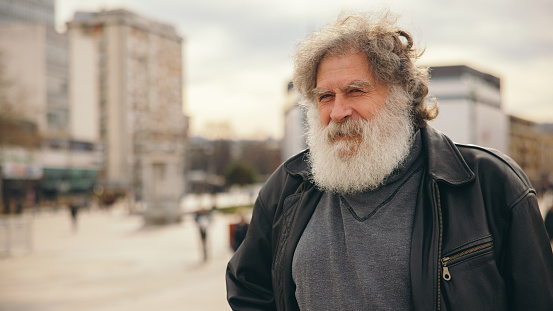 Portrait of an senior Caucasian man with an long gray hair and beard, wearing black leather jacket, in the city