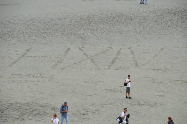 Sand writing in Mont Saint Michel\nSand around the hill\n08/05/2014\n\nMont Saint Michel, France. 8th May 2014 at 14:17. Sand writings in the surroundings of the Mont Saint Michel when the tide is low and turists walking around and taking pitures.