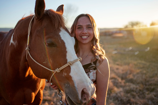 Pretty Young Caucasian Woman Smiling with Her Quarter Horse with Hazy Light in a Grassy Field at Sunset