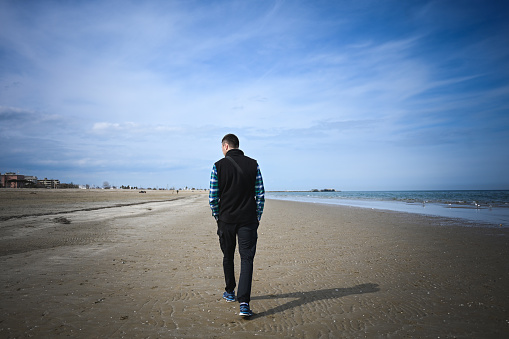 Rear view of a tourist walking on an empty beach.