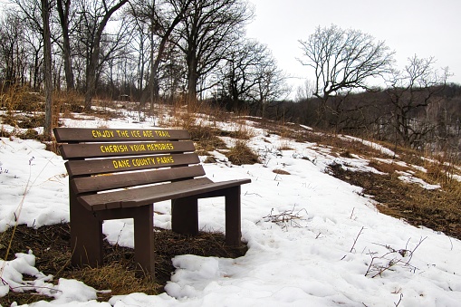 An empty wooden bench displays welcoming text on a Winter day along the Springfield Hill Segment of the Ice Age Trail, near Springfield Corners, Wisconsin.