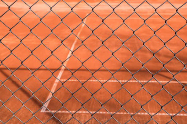 Red clay tennis court surface seen through chain link metal fence