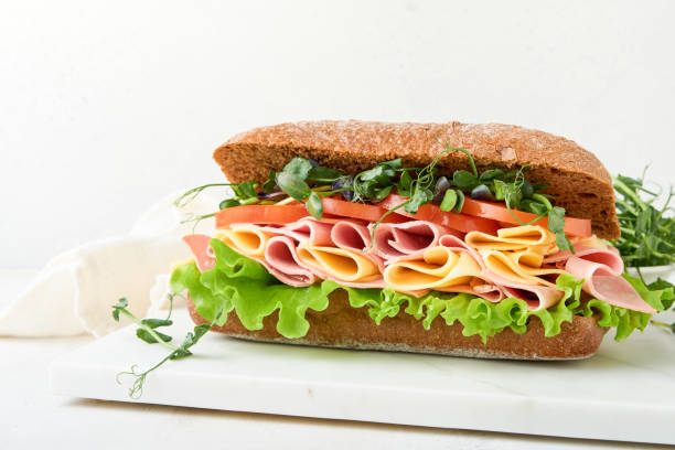 istock Sandwich. One fresh big submarine sandwich with ham, cheese, lettuce, tomatoes and microgreens on light background. Healthy breakfast theme concept, school lunch, breakfast or snack. 2120180948