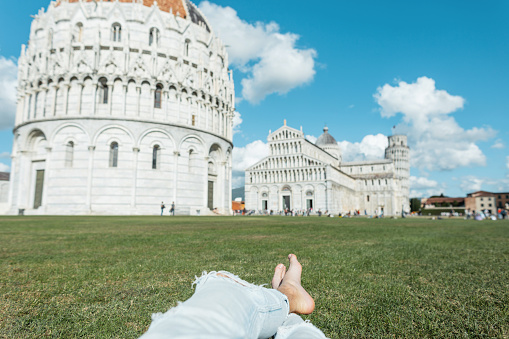 Traveling man lying and rest on the grass and famous on the popular architecture with towers and churches in Pisa, Italy. Travel and vacation in Europe, Italy