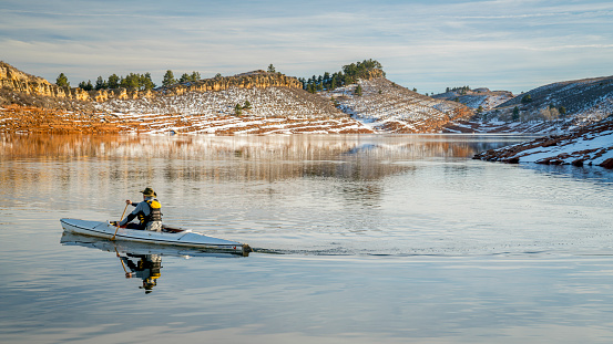 senior male wearing life jacket is paddling expedition canoe in winter scenery of Horsetooth Reservoir in northern Colorado - self portrait