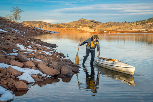 senior male wearing life jacket is paddling expedition canoe in winter scenery of Horsetooth Reservoir in northern Colorado. Self portrait.