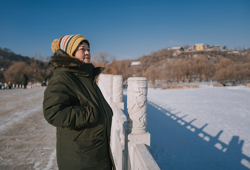 Asian Chinese female tourist standing on bridge looking at frozen lake in Jilin public park