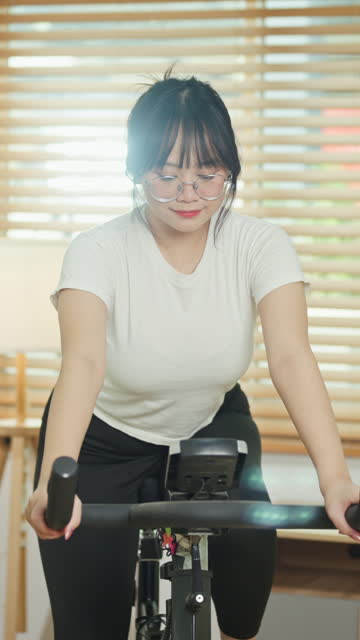 Pretty young Asian woman doing cardio on stationary bike at home. Healthy lifestyle concept.