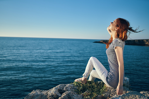 woman in a t-shirt and trousers sits on a stone near the sea in summer. High quality photo