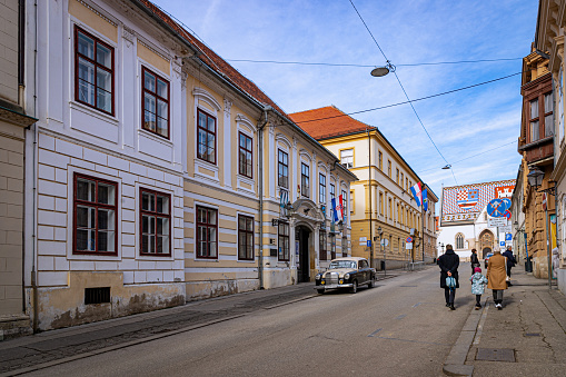 February 3rd, 2024. Zagreb,  Old style car parked in the street and family walking towards the national monument.