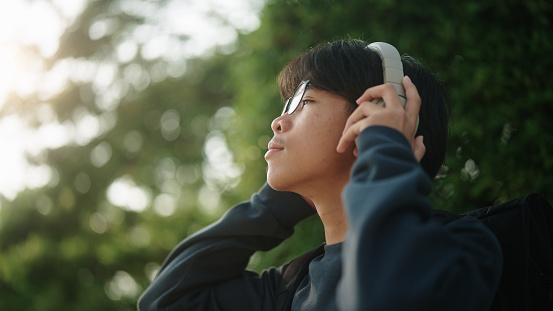 Asian teenage boy wearing headphone at green environment.