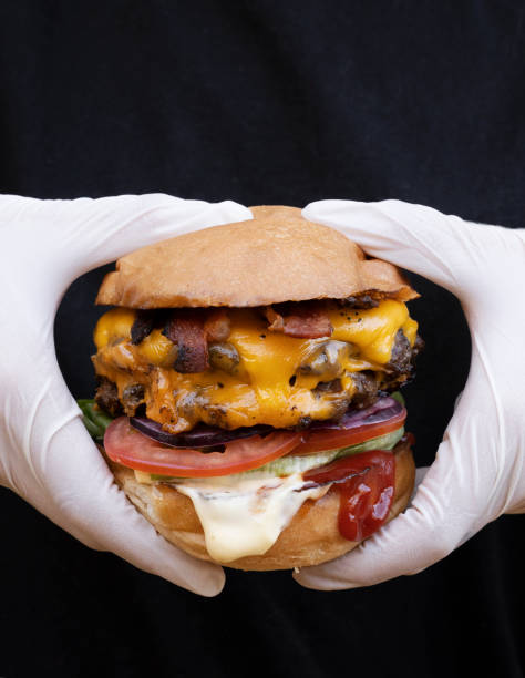 istock Closeup view of a chef wearing white gloves presenting a multilayer burger with cheddar cheese 2120473840