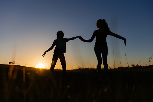 Silhouette of a mother and son dancing in a field at sunset