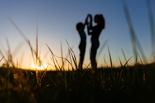 Silhouette of a mother and son dancing in a field at sunset