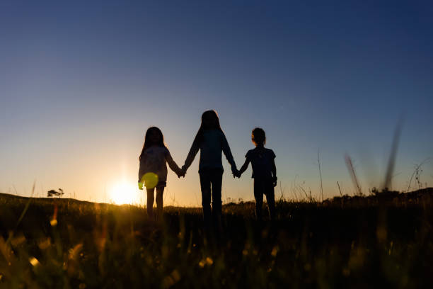 istock Silhouette of three siblings at sunset in a field 2120477166