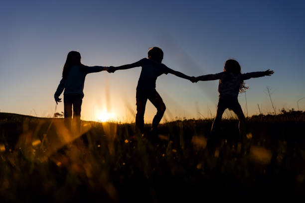 istock Silhouette of three siblings at sunset in a field 2120478495