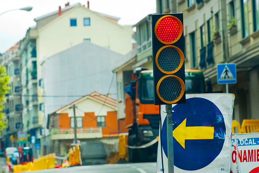 Red traffic light, traffic arrow sign, road construction, street view. City life, Galicia, Spain.