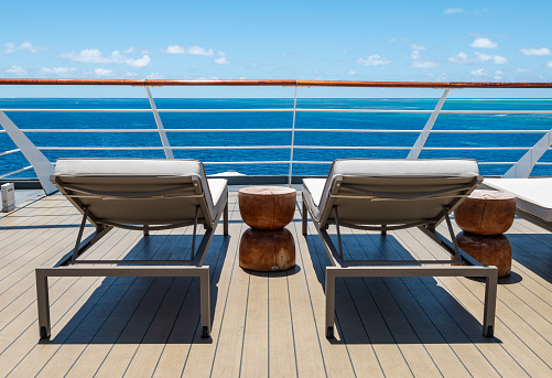 Travel image with two stylish deck chairs on wooden deck of cruise ship, at railing, with sea view on beautiful summer day. No people.