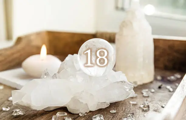 Number eighteen on gemstone sphere or crystal ball known as crystallum orbis or orbuculum. Natural clear quartz ball on stand on wood tray in home. Predictions concept.