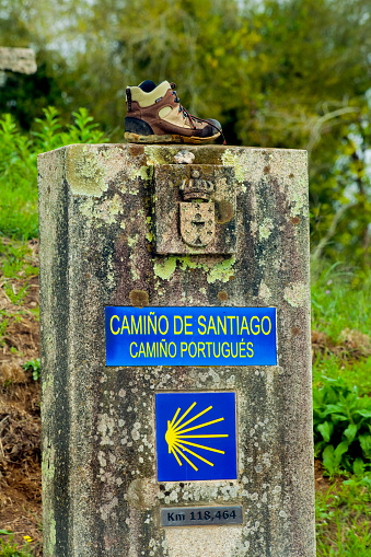 Camino de Santiago sign, multicolored tiles, scallop symbol, Camino portugués. Tui, Galicia, Spain.Pilgrimage route to Santiago de Compostela, UNESCO world site heritage. Green grass in the background. Hiking boot on the milestone.