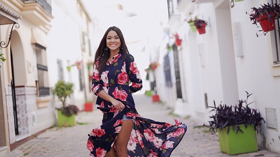 A carefree young woman in a beautiful floral dress twirling on a quaint street in Spain, embodying joy and freedom.