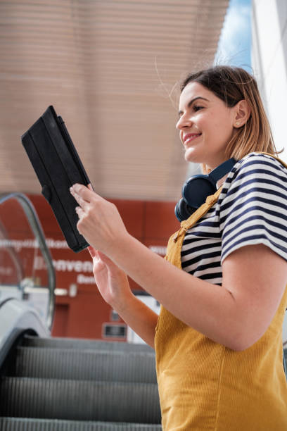 istock Young woman in yellow dungarees using the tablet to update her email while commuting to work. Concept: lifestyle, fashion, outdoors. 2120594149