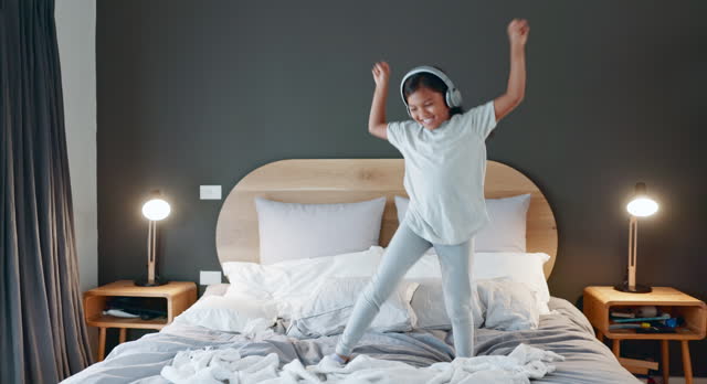 Young girl, dancing and bed at home with music and happy from song in morning. Youth, dancer and headphones with dancer and comedy in a house bedroom with a child and energy of a kid with audio