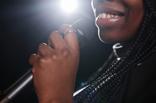 Close up of smiling Black woman holding microphone on stage with spotlight copy space