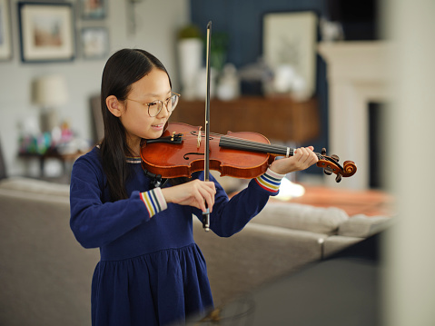 A young Korean Asian girl practicing violin in a home.